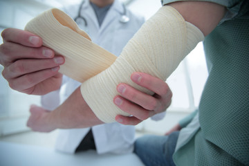 Orthopedist applying bandage onto patient's hand in clinic
