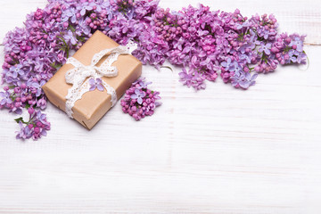 Obraz na płótnie Canvas Lilac flowers and cute gift box on white wooden background, copy space. Mother's day background