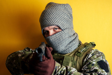 terrorist man in camouflage and mask on a yellow background. the concept of anonymity and terrorism pistol gun