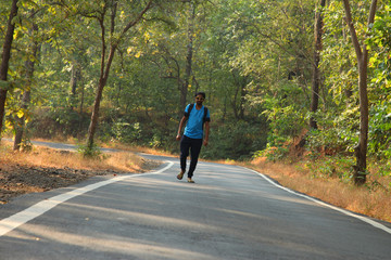 Travel concept man carrying backpack walking on the road passes through beautiful forests.