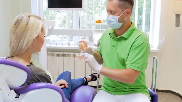 4k footage of dentist showing plastic model of teeth to his patient
