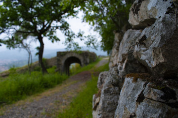 Sentiero di campagna lungo le mura di un castello, con ponte romano in lontananza - obrazy, fototapety, plakaty