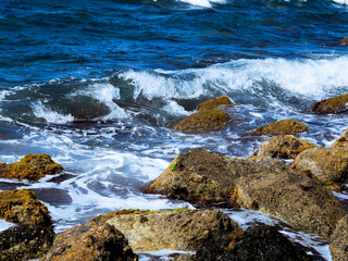 Splashes from the waves bumping against the rocky shore, The sea is dark blue with white spray