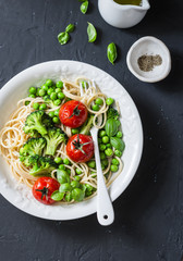 Veggie pasta. Vegetarian lunch - spaghetti with broccoli cabbage, green peas and cherry tomatoes on dark background, top view. Healthy  food concept