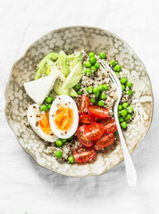 Morning savory breakfast bowl. Balanced bowl with quinoa, egg, avocado, tomato, green pea. Healthy diet food concept. Top view, on light background