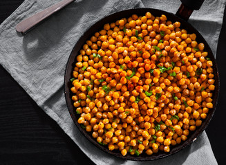 Fried spicy chickpeas in frying pan on wooden table.