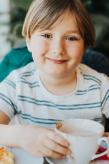 Funny little boy drinking hot chocolate for breakfast