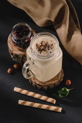 closeup view of glass with milkshake on wooden slice, currants, walnuts, mint, sweet straws and kitchen towel