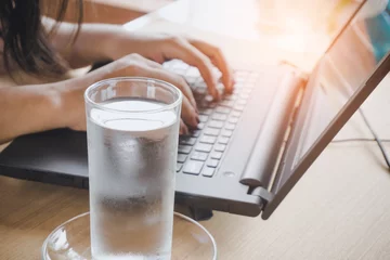 Foto auf Acrylglas Geschäftsfrau, die frisches Wasser trinkt, während sie am Computer-Laptop am Schreibtisch arbeitet © doucefleur