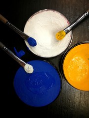 Синяя, желтая и белая краски и кисти на черном фоне. 