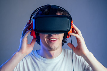 portrait of a young man in the glasses of virtual reality on a gray wall background. The concept of games in the mask of virtual reality