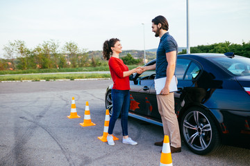 Driving school or test. Beautiful young woman with instructor learning how to drive and park car between cones.