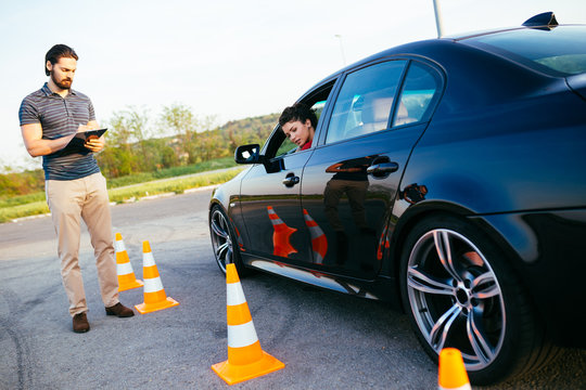 Driving school or test. Beautiful young woman with instructor learning how to drive and park car between cones.