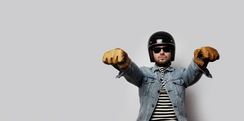 Foto op Plexiglas Young biker in a blue denim jacket pretending to ride a motorcycle isolated on white background. Horizontal. Wide © KleverLevel