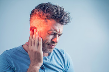 male having ear pain touching his painful head isolated on gray background - obrazy, fototapety, plakaty