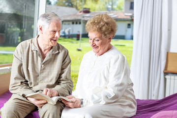 Elder couple reading book at home seated on the bed