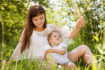 Mother with baby daughter blowing to dandelion in park.