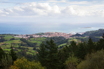 Fototapeta na wymiar Scenic views of green landscape with Bermeo fishing town by the sea on the background, Basque Country
