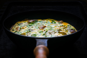 Scrambled eggs with herbs, bread, meat, onions and garlic in a frying pan on a dark background. Low key. Selective focus