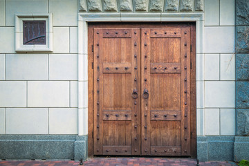 Heavy doors made of wooden boards with round handles against the gray wall