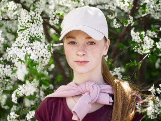 Beautiful young redhead woman enjoying spring in blossoming garden. Close up portrait.