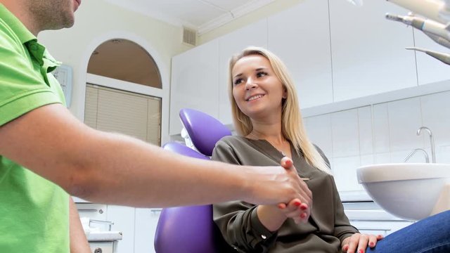 4k footage of happy smiling woman sitting in dentist chair and shaking hands with doctor