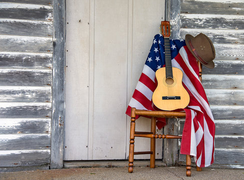 brown hat and six string guitar on wooden chair with American flag by weathered wooden door