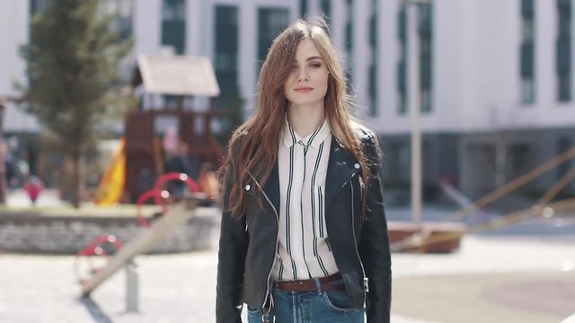 a young fashionable girl walks through the spring city in the sun. portrait of a beautiful young woman against a background of modern architecture. slow motion