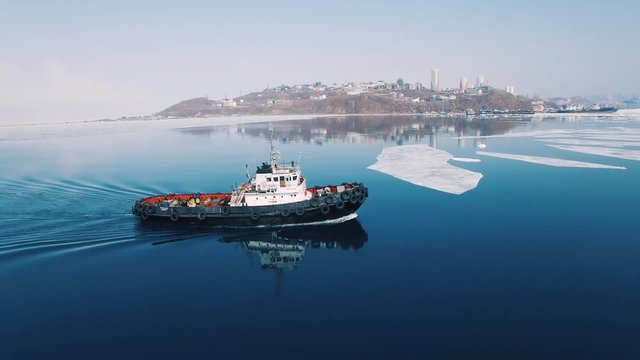 A towboat goes among the ice on the background of the city