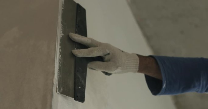 Slow motion pan of worker applying putty on the wall