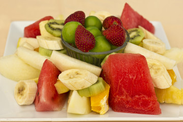 Fruits on a plate. Green plum, strawberry, banana, kiwi, watermelon, orange and apple.