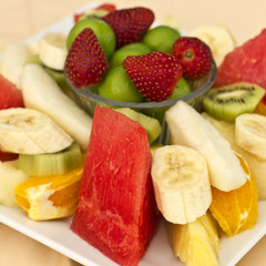 Fruits on a plate. Green plum, strawberry, banana, kiwi, watermelon, orange and apple.