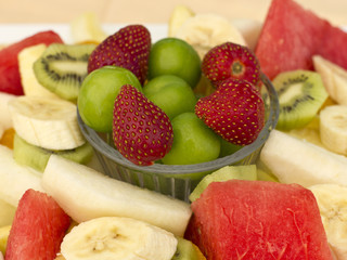Fruits on a plate. Green plum, strawberry, banana, kiwi, watermelon, orange and apple.