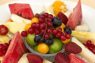 Fruits on a plate. Green plum, red currant, blueberry, strawberry, physalis, pitahaya, watermelon, orange and apple.