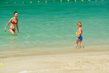 Toddler boy playing on beach with mother