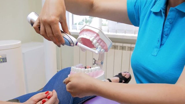 Closeup 4k video of dentist showing how to use electric brush while cleaning teeth