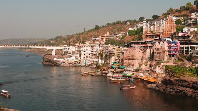 Omkareshwar cityscape, India, sacred hindu temple. Holy Narmada River, boats floating. Travel destination for tourists and pilgrims. 