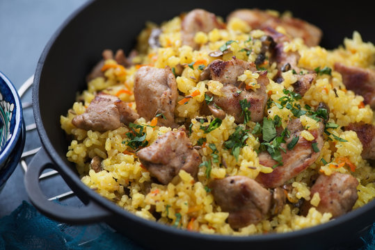 Close-up of pilaf with pork meat and mushrooms in a cast-iron pan, selective focus, horizontal shot