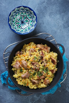 Cast-iron pan with pilaf on a blue stone background, vertical shot, above view