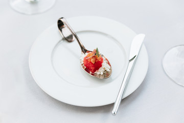 Modern French food: Diced watermelon with white crush cheese served in silver spoon on white plate with cutlery as appetizer.