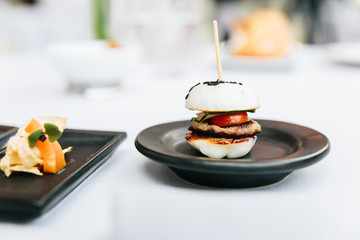 Modern French appetizer: Mini hamburger including white bun, pork, sliced cucumber, tomato and raddish topping with black sesame.