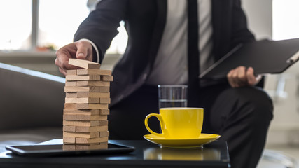 Businessman sitting in office building a tower of stacked blocks of wood