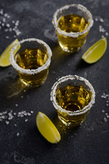 Gold tequila with lime and salt rim on dark stone or concrete background, selective focus