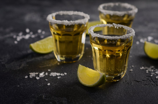 Gold tequila with lime and salt rim on dark stone or concrete background, selective focus
