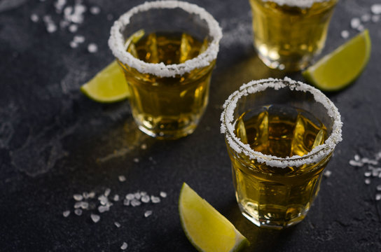 Gold tequila with lime and salt rim on dark stone or concrete background, selective focus