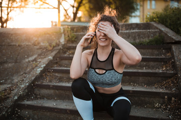 Young woman in sportswear is sitting on stairs outdoors. She is reminded that she had forgotten to go on coffee.