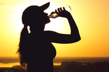silhouette of a woman drinking water after physical exercise in nature, sports female profile at...