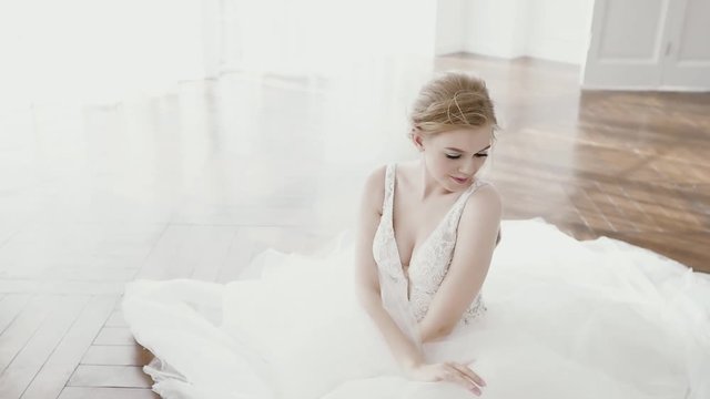 Beautiful bride in a gorgeous dress and bridal veil stands by the window dreaming, smiling charmingly. Happy moments, couple goals, morning of a bride