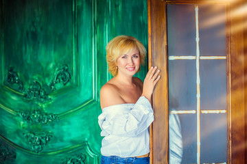 Fototapeta premium Portrait of blond woman in white shirt with bared shoulders standing at door in background of green wall