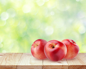 Three nectarines on a wooden table on blurred nature background.